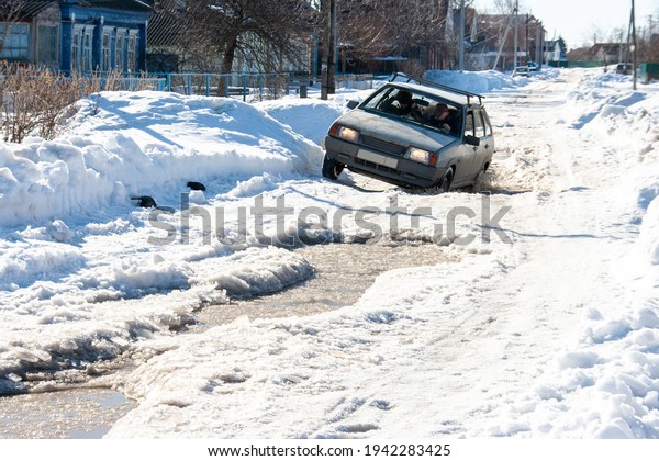 A car on a road with deep puddles from melting snow\
at the end of March
