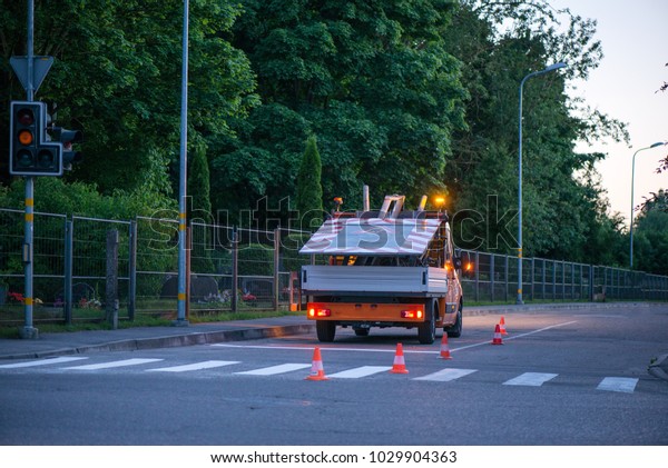 Car on side of road with warning lights. Road\
construction works. Traffic line painting. Painting white street\
lines on pedestrian crossing. Road cones with orange, white stripes\
standing on asphalt. 