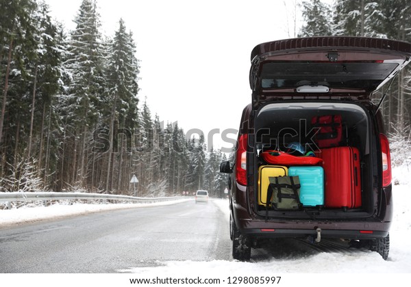 Car with open trunk full of luggage near road,\
space for text. Winter\
vacation