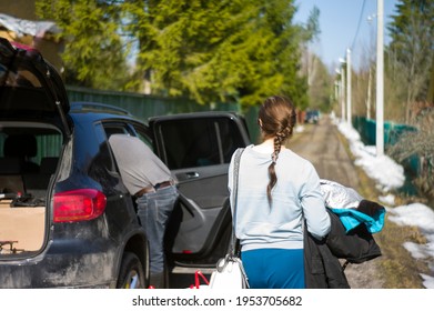 A Car With Open Trunk And A Woman Waiting For Her Friend Arranging Baggage On A Backseat