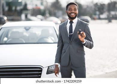 Car Owner. Happy African Businessman Showing New Auto Key Standing Near His Luxury Automobile Outdoors. Copy Space