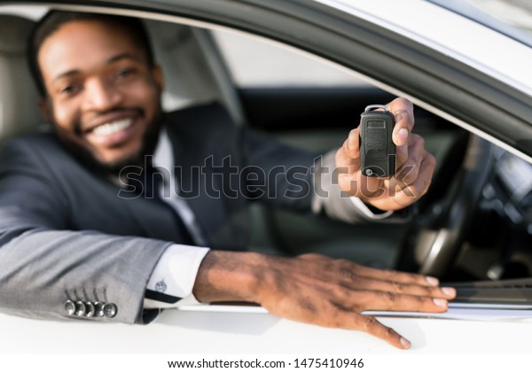 Car owner. Happy man showing key, sitting in auto
and smiling to camera