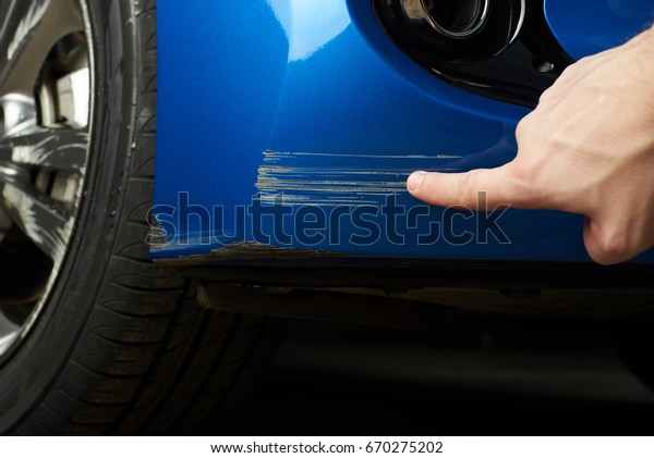 Car paint scratch close-up. Finger show scratch on\
blue car