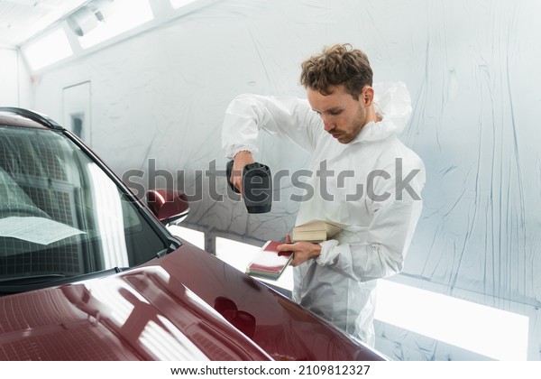 Car painter man determines the correct tone of a\
vehicle body colour using a special colorist\'s lamp. Auto body\
repairman in garage