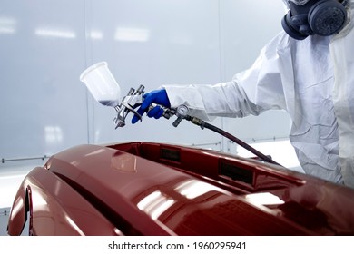 Car Painter In Protective Clothes And Mask Painting Automobile Bumper With Metallic Paint And Varnish In Chamber Workshop.