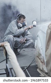 Car painting and automobile repair service. Auto mechanic in white overalls paints car with airbrush pulverizer in paint chamber