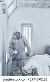 Car Painting And Automobile Repair Service. Auto Mechanic In White Overalls Paints Car With Airbrush Pulverizer In Paint Chamber
