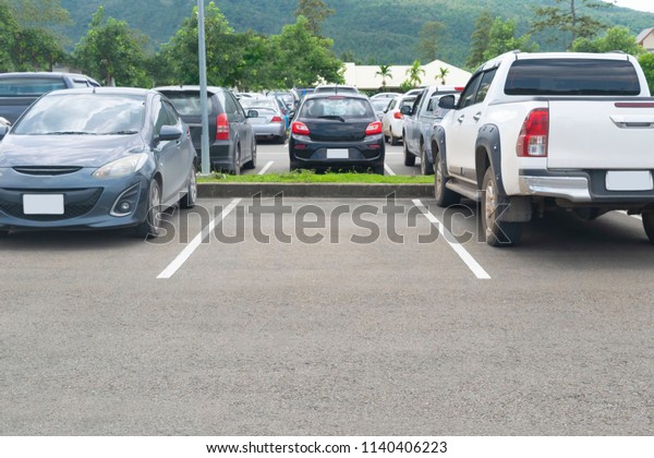 Car\
parked in asphalt parking lot and a empty space parking space in\
nature with trees, beautiful cloudy sky and mountain background\
.Outdoor parking lot with green environment\
concept\
