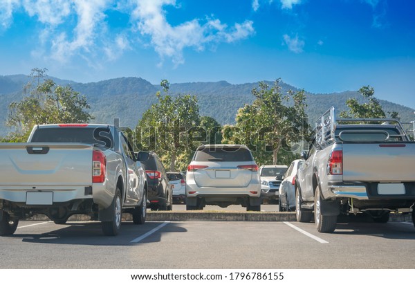 Car parked in asphalt parking lot and empty\
space parking with trees, sun, mountain, blue sky background.\
Outdoor parking lot with fresh nature, green environment\
transportation and\
technology\
