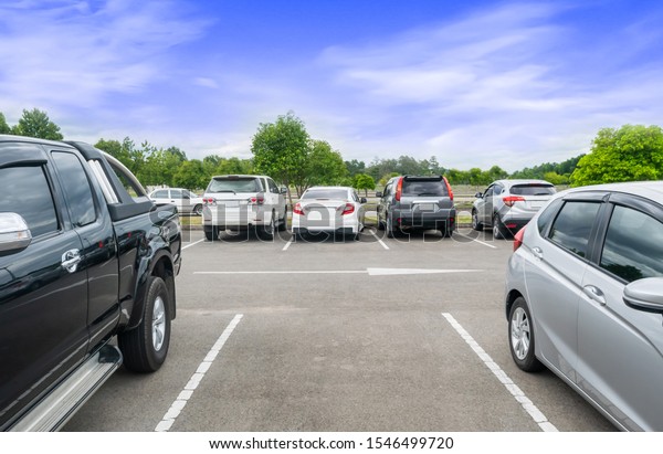 Car parked in asphalt parking lot, white cloud\
and blue sky background, one empty space parking. Outdoor parking\
lot with fresh  and green environment. Travel transportation\
technology concept\
