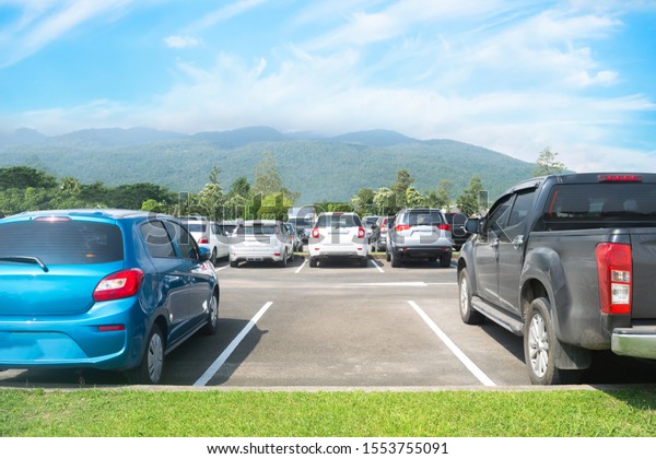 Car parked in asphalt parking lot. Trees,\
mountain, blue sky background, empty space parking. Outdoor parking\
lot with green environment. Travel transportation technology with\
nature concept\
\
