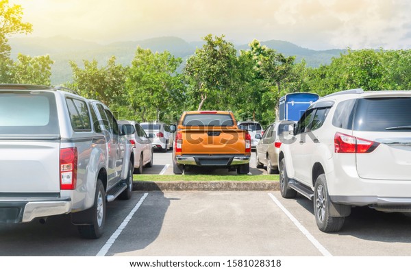 Car parked in asphalt parking lot. Trees,\
mountain, blue sky background, empty space parking. Outdoor parking\
lot with green environment. Travel transportation technology with\
nature concept\
