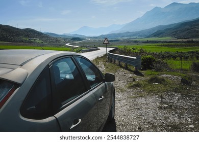 A car is parked by the roadside, gazing at the stunning Albanian landscape, where winding roads ascend into the mountains and quaint villages. Travel photo, Nobody. - Powered by Shutterstock