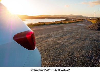 Car Parked By A Small Lake With Blue Water And Wild Fields. Beautiful Sun Rise Scene In Connemara, County Galway, Ireland. Warm And Cool Tones. Haze Over Mountains In The Background.