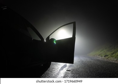 A Car Parked, With Door Open, On The Side Of The Road, Underneath A Street Light. On A Foggy Winters Night