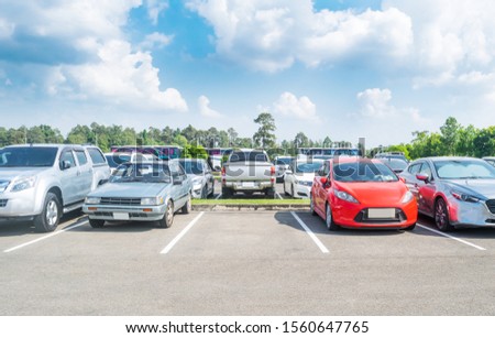 Car parked in large asphalt parking lot with trees, white cloud  and blue sky background. Outdoor parking lot with fresh ozone and green environment of travel transportation concept
