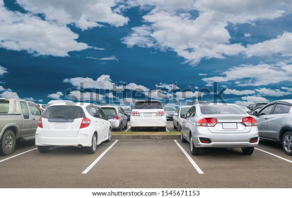 Car parked in large asphalt parking lot,\
white cloud and blue sky background, one empty space parking.\
Outdoor parking lot with fresh  and green environment. Travel\
transportation technology\
concept\
\
