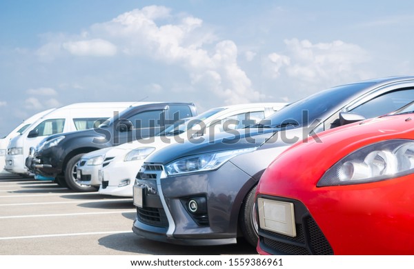 Car parked in large asphalt parking lot in a\
row with white cloud and blue sky background. Outdoor parking lot\
with fresh ozone and green environment of travel transportation\
technology concept\
