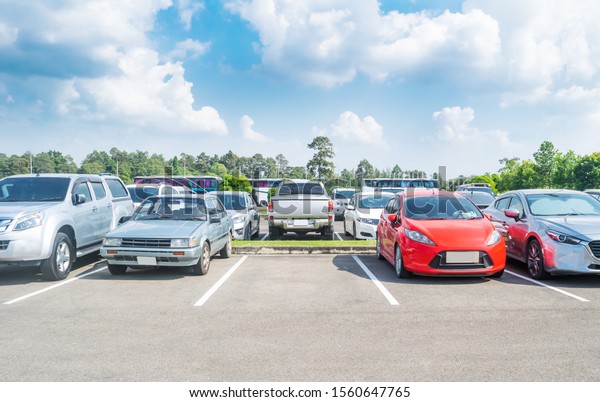 Car parked
in large asphalt parking lot with trees, white cloud  and blue sky
background. Outdoor parking lot with fresh ozone and green
environment of travel transportation
concept
