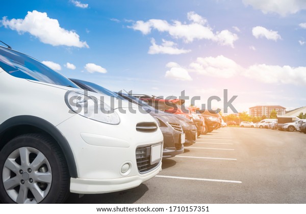 Car parked in large asphalt parking lot in a\
row with beautiful sky background. Outdoor parking lot with nature\
fresh ozone and green environment of travel transportation business\
concept\
