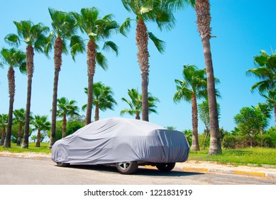 The car is in the parking with auto cover from the sun surrounded by palm trees. Hot countries, protection from heating the car.