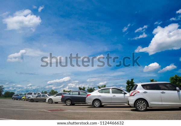 Car\
parking in large asphalt parking lot with trees, white cloud and\
beautiful blue sky background in sunny day. Outdoor parking lot\
with fresh ozone and green environment\
concept