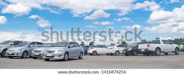 Car parking in large asphalt parking lot with trees,\
white cloud and blue sky background in sunny day. Outdoor parking\
lot with fresh ozone and green environment of transportation and\
technology \
 