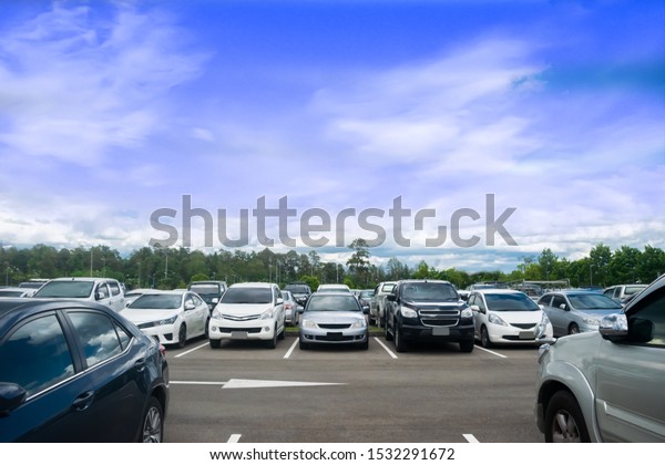 Car parking in\
large asphalt parking lot with trees, white cloud and blue sky\
background. Outdoor parking lot with fresh ozone and green\
environment of transportation\
concept\
