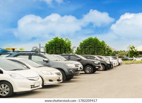 Car\
parking in large asphalt parking lot with trees, white cloud and\
blue sky background in front of hall building. Outdoor parking lot\
with fresh ozone and green environment\
concept