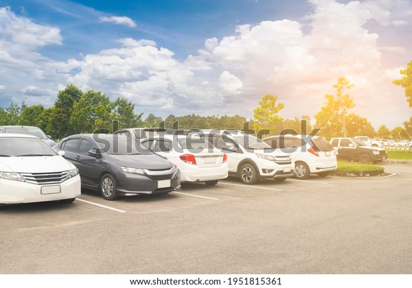 Car parking in\
large asphalt parking lot with trees, white cloud and blue sky\
background. Outdoor parking lot with fresh ozone and green\
environment of transportation\
concept\

