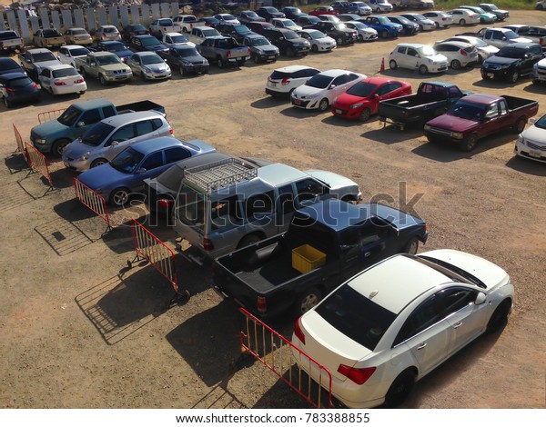 Car parking in parking lot. Row of various cars\
parked at outdoor parking lot on the soil ground background under\
sunlight, birds eye view\
