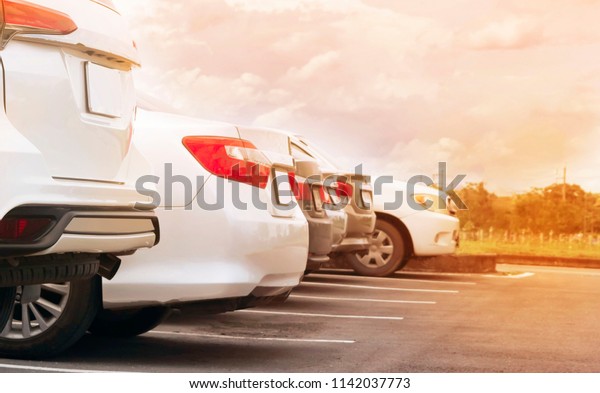 Car parking\
in parking lot. Row of white cars parked at outdoor asphalt parking\
lot with cloudy sunset sky\
background