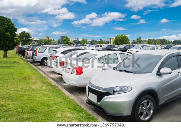 Car parking in parking lot. Row of white\
cars parked at outdoor  parking lot near grass pavement, white\
cloud and blue sky\
background\
