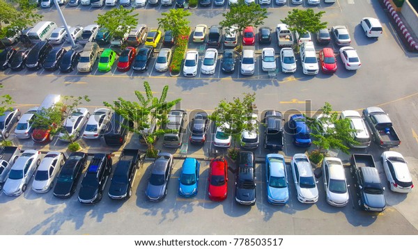 A lot of car parking in\
outdoor parking lot,Many tree plant and grow in car park, yellow\
direction arrow on the street. Exhibition or Department store car\
park.