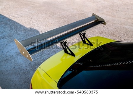 car part ; Close up detail of a custom racing carbon fiber spoiler on the rear of a yellow car