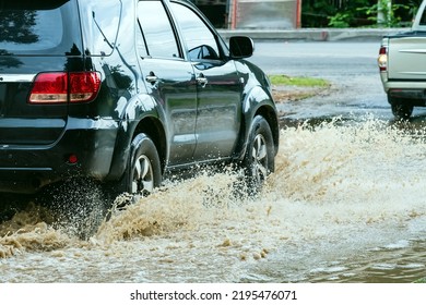 Car passing through a flooded road. Driving car on flooded road during flood caused by torrential rains. Flooded city road with a large puddle. Splash by car through flood water. Selective focus. - Shutterstock ID 2195476071