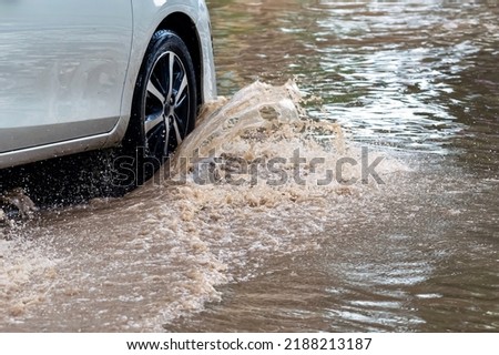 Car passing through a flooded road. Driving car on flooded road during flood caused by torrential rains. Flooded city road with a large puddle. Splash by car through flood water. Selective focus. Stock photo © 