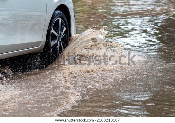 Car passing through a flooded road. Driving car on\
flooded road during flood caused by torrential rains. Flooded city\
road with a large puddle. Splash by car through flood water.\
Selective focus.