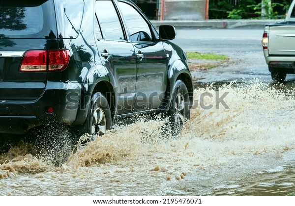 Car passing through a flooded road. Driving car on
flooded road during flood caused by torrential rains. Flooded city
road with a large puddle. Splash by car through flood water.
Selective focus.