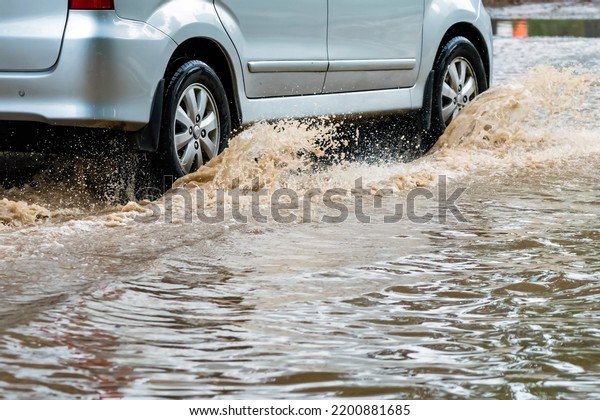 Car passing through a flooded road. Driving car on\
flooded road during flood caused by torrential rains. Flooded city\
road with a large puddle. Splash by car through flood water.\
Selective focus.