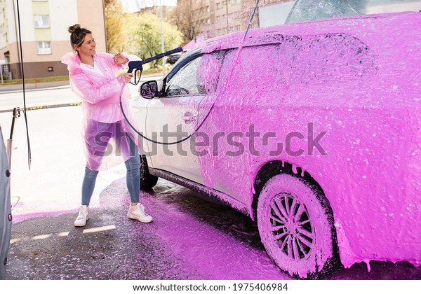 Car in pink foam at self-service car\
wash, woman worker happily doing her job, stock\
photo