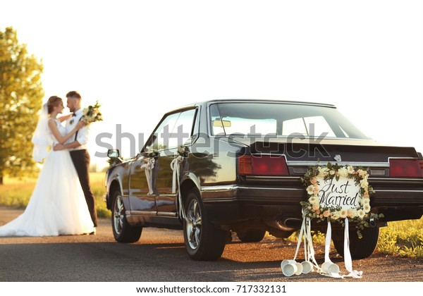 Car with plate JUST MARRIED and happy wedding\
couple outdoors