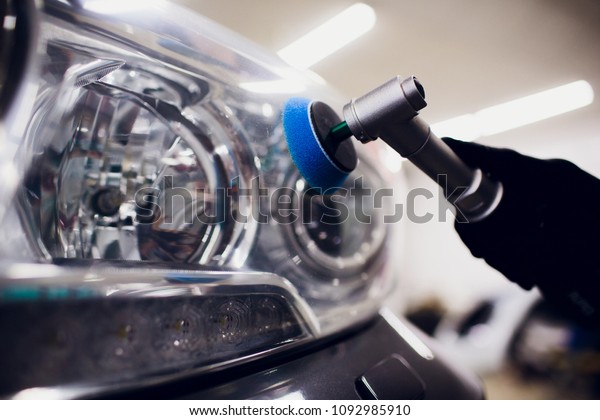 Car polish\
wax worker hands holding polisher and polish car detailing or\
valeting concept front white auto\
headlight