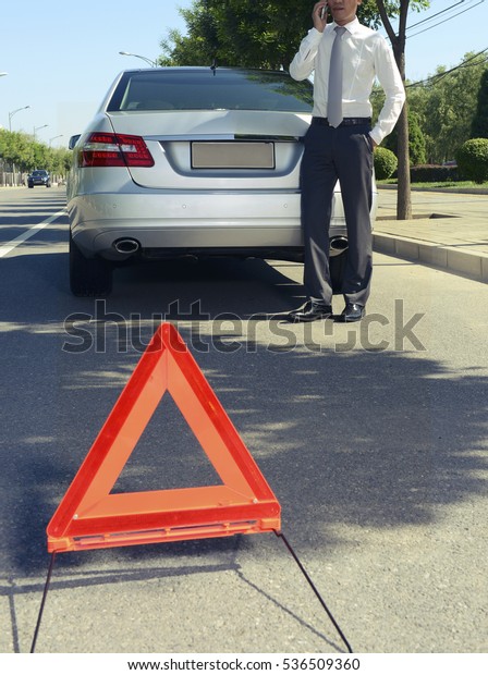 Car with problems and men awaiting\
recovery services , red triangle to warn other road\
users