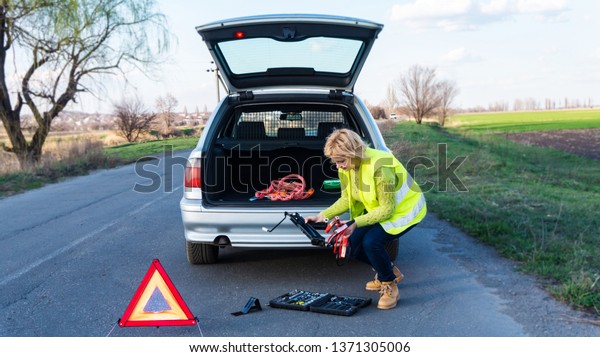Car problems, red warning\
triangle! Young woman with warning triangle on street . Girl\
repairing car