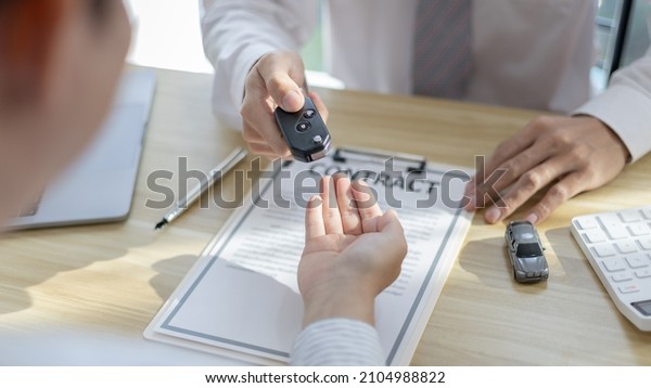 Car purchase contract and\
insurance, Man attendant handed over the car key to the customer\
who signed the contract and the terms of the agreement on the\
document.