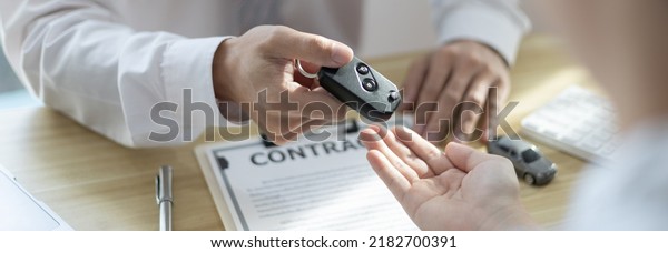 Car purchase contract and\
insurance, Man attendant handed over the car key to the customer\
who signed the contract and the terms of the agreement on the\
document.