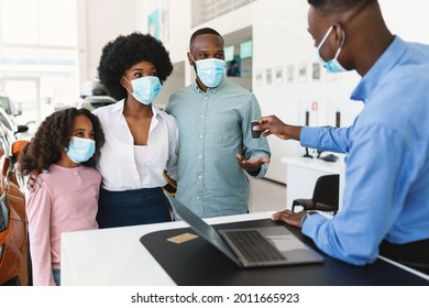 Car Purchase During Covid Lockdown. Afro Family In Face Masks Taking Electronic Car Key From Salesman At Auto Dealership. Black Clients Buying Or Renting New Vehicle At Showroom Shop