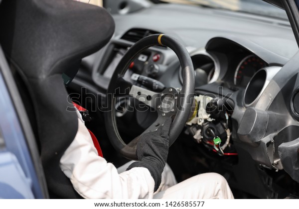 Car racer wearing protective leather and helmet\
holding a steering wheel
