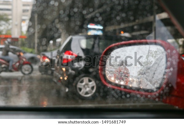 Car in rainy day. Rain drops\
on car window. Be careful and safe drive in bad weather. Traffic\
jam on the road side view. People ride motorcycle in side\
mirror.